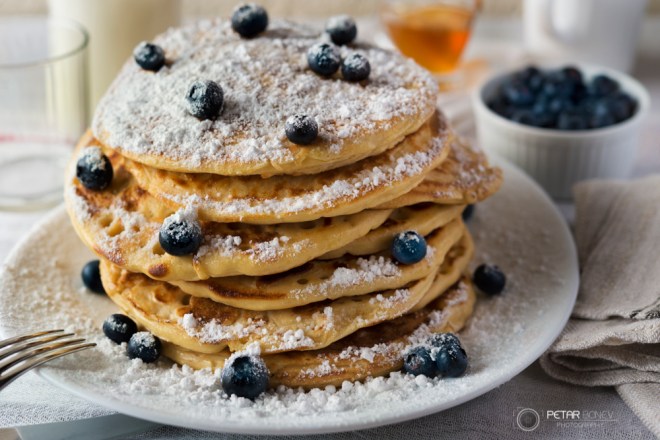 Tasty breakfast of pancakes with blueberries, powdered sugar, milk and honey